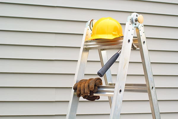 a ladder with a hard hat, gloves, and a hammer resting on it in front of a home