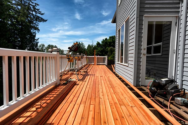 A long view of a tan wooden deck being built with a white railing.