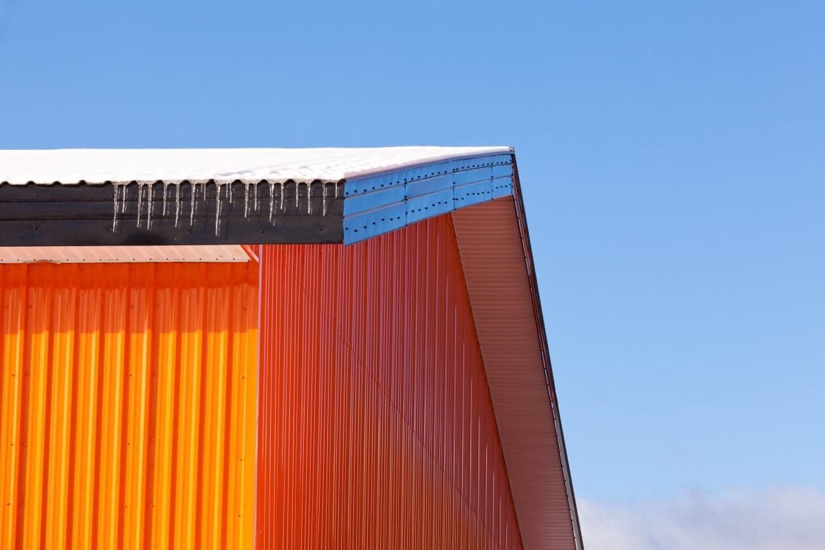 A building with bright orange metal siding and snow peaking over the roofing