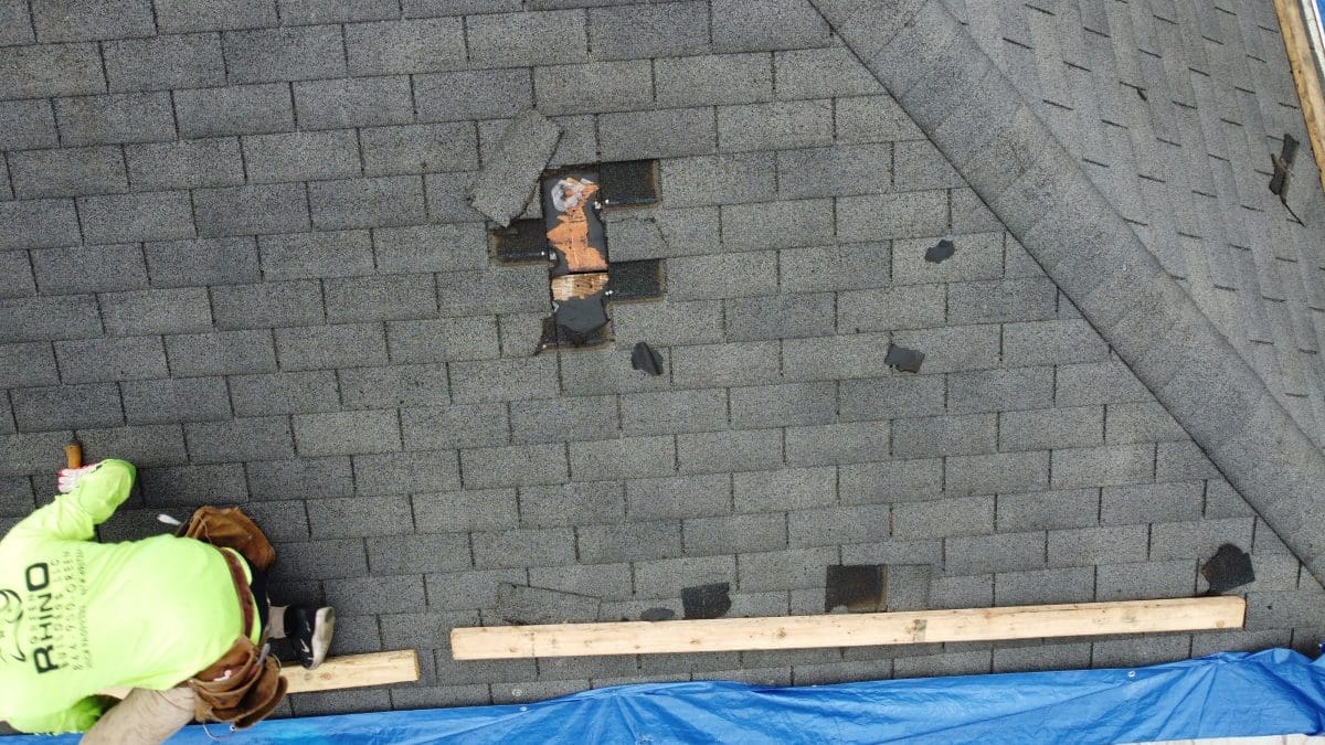 A spot on a residential roof with missing shingles and a Green Rhino roofer in the corner.