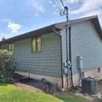 A view of the back corner of a house with blue-green siding materials.